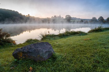 Church on the hill with lake in foreground. Autumn foggy morning with the first frost. Bysicka church near SPA town Lazne Belohrad, Czech Republic. clipart