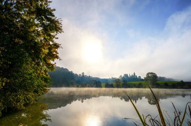 Romantic landscape with small church on the hill reflected in the pond. Autumn morning day with fog. St. Peter and Pauls church at Bysicky near Lazne Belohrad, Czech Republic. clipart