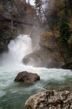 Slovenya 'nın Vintgar vadisinin sonundaki Radovna nehrinde sonbahar sel baskınında Picturesque Sum şelalesi. Vintgar Gorge ünlü Bled Lake yakınlarında popüler bir turistik merkezdir.
