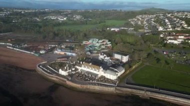 Goodrington Sands, Devon, İngiltere: DRONE VİEWS: Brewers Fayre barından uzaklaşın, Splashdown Quaywest su parkı flume gezileri, Premier Inn oteli; Daireler Young 's Park' ın kayıkhane göllerini, Paignton kasabasını gözler önüne sermek için; barın yukarıdan görünüşü, akışkan binişler ve otel manzarası.