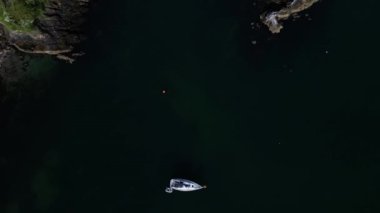 Churston Cove, Torbay, Güney Devon, İngiltere: DRONE AERIAL VİEWS: İHA, kıyıya demirlemiş tek bir yatın doğrudan tepeden görünüşünü gösteriyor; İHA Churston Koyu 'nu ve yakındaki kayalıkları ve engebeli kıyı şeridini ortaya çıkarmak için ileri doğru uçuyor.