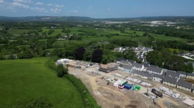 Newton Abbot, Güney Devon, İngiltere: DRONE AERIAL VieWS: Pan r-to-l, yeşil kuşak arazisinde kısmen inşa edilmiş evleri, tamamlanmış evleri ve temelleri olan yeni bir inşaat alanı. Dartmoor Milli Parkı 'na doğru bakan kırsal bölge (Clip 1).