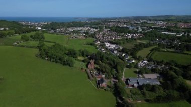 Collaton St Mary, Güney Devon, İngiltere: DRONE AERIAL VİEWS: İHA yeşil kuşak üzerinden Collaton St. Mary ve St Mary kilisesine doğru uçar; arka planda ise kıyı kenti Paignton ve Torbay deniz / kıyı şeridi bulunur..