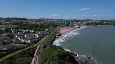 Goodrington Sands, Paignton, Torbay, Devon, İngiltere: DRONE VİEWS: Hava aracı güneşli bir yaz gününde Goodrington Sands 'e doğru uçuyor, tatilciler / turistler sahilde güneşleniyor ve denizde yüzüyor.