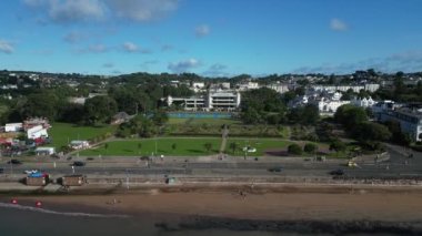 Torquay, Torbay, Güney Devon, İngiltere: DRONE ViEWS: Torquay sahili boyunca uzanan insansız hava aracı, Torre Abbey Gardens 'taki Riviera Uluslararası Merkezi, ana yol trafiği ve yaz lunaparkını gösteriyor. Torquay İngiltere 'de büyük bir tatil ve turizm merkezidir (Clip 2).