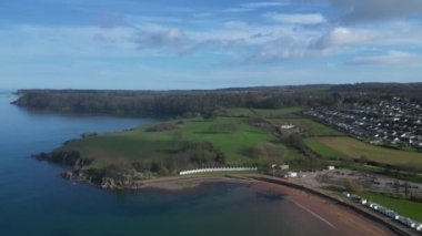 Broadbay, Torbay, Güney Devon, İngiltere: İHA kamerası Broadsand sahili ve Torbay kıyı şeridini göstermek için sahil kulübelerine doğru uçarken aşağı doğru eğiliyor. Torbay popüler bir İngiltere tatil beldesidir (Clip 2).