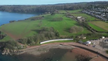 Broadbay, Torbay, Güney Devon, İngiltere: DRONE VİEWS: İnsansız hava aracı kameraları Broadsand plajı ve Torbay kıyı şeridini göstermek için sahil kulübelerinden uzaklaşırken yukarı doğru eğiliyor. Torbay popüler bir İngiltere tatil beldesidir (Clip 1).