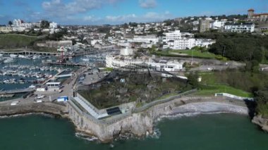 Torquay, Torbay, Güney Devon, İngiltere: DRONE VİEWS: İnsansız hava aracı eski turizm merkezi Living Coast 'u (ağ ile kaplanarak), Torquay Marina' yı ve çevresindeki yamaçtaki mülkleri çevrelemektedir. Torquay popüler bir İngiltere tatil beldesidir (Clip 3).