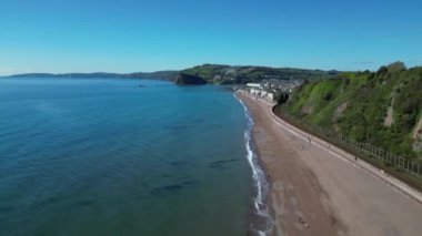 Teignmouth, Güney Devon, İngiltere: DRONE VİEWS: İnsansız hava aracı uzun, kumlu bir sahil boyunca batıya, Teignmouth İskelesi 'ne doğru uçar; Teignmouth kasabası görüntüye girer (resmin sağında). Teignmouth hem bir liman hem de popüler bir İngiltere tatil beldesidir..