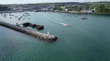 Brixham, Torbay, Güney Devon, İngiltere: DRONE VİEWS: Bir RNLI cankurtaran botu liman deniz fenerinde denize doğru yol alırken. Brixham hem büyük bir balıkçılık limanı hem de popüler bir İngiltere tatil beldesidir (Clip 1).