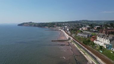 DRONE VİEWS: İHA, ana demiryolu hattı boyunca doğuya, deniz savunma duvarına ve kumlu plajların üzerinden uçuyor. Teignmouth hem bir liman hem de popüler bir İngiltere tatil beldesidir (Clip 1).
