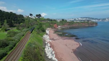 Hollicombe, Torquay, Torbay, Güney Devon, İngiltere: İHA Hollicombe sahilinde uçarken yerel bir tren Paignton 'a doğru ilerliyor. Torbay, pek çok farklı turistik mekanı bulunan popüler bir İngiltere tatil beldesi..