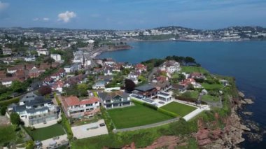Hollicombe, Torquay, Torbay, Güney Devon, İngiltere: DRONE VİEWS: İHA yukarı ve yukarı pazar evleri ve körfezin karşısındaki Torquay kasabasını ortaya çıkarmak için kızıl kumtaşı uçurumları üzerinde yükselir. Torbay popüler bir İngiltere tatil beldesidir (Clip 1).