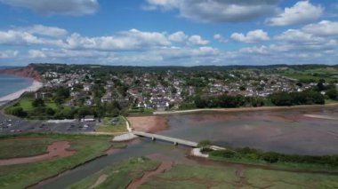 Budleigh Salterton, Devon, İngiltere: DRONE VİEWS: İHA arka planda Jurassic Coast ve Budleigh Salterton 'ı gösteren nehir samuru üzerinde bir köprü etrafında daireler çiziyor. Jurassic Coast popüler bir İngiltere turizm merkezidir (Clip 1).