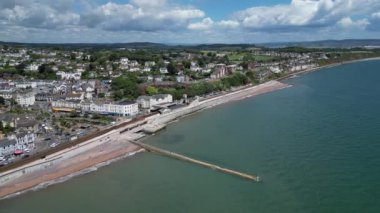 Dawlish, Güney Devon, İngiltere: DRONE VİEWS: İHA şehir merkezini, yeni deniz savunma duvarlarını, tren istasyonunu ve kıyı şeridini gösteren Dawlish şehir rıhtımında daireler çiziyor. Dawlish İngiltere 'de popüler bir tatil beldesidir ve yerel siyah kuğularıyla tanınır (Clip 1).
