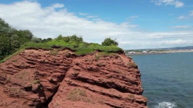 Dawlish Warren, River Exe, Güney Devon, İngiltere: DRONE VİEWS: İnsansız hava aracı, Dawlish Warren, dönme dolap, tren yolu ve Exe Nehri 'ni ortaya çıkarmak için kırmızı kumtaşı uçurumlarının üzerinden yükselir. Güney Devon popüler bir İngiltere tatil beldesidir (Clip 2).