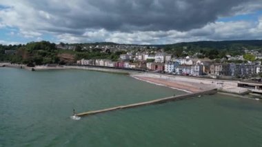 Dawlish, Güney Devon, İngiltere: DRONE VİEWS: İHA şehir merkezini, yeni deniz savunma duvarlarını, tren istasyonunu ve kıyı şeridini gösteren Dawlish şehir rıhtımında daireler çiziyor. Dawlish İngiltere 'de popüler bir tatil beldesidir ve yerel siyah kuğularıyla tanınır (Clip 1).