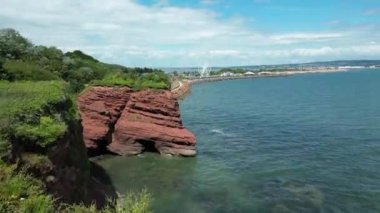 Dawlish Warren, River Exe, Güney Devon, İngiltere: DRONE VİEWS: İnsansız hava aracı, Dawlish Warren, dönme dolap, tren yolu ve Exe Nehri 'ni ortaya çıkarmak için kırmızı kumtaşı uçurumlarının üzerinden yükselir. Güney Devon popüler bir İngiltere tatil beldesidir (Clip 1).