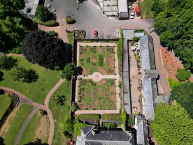 Cockington, Torbay, South Devon, England: DRONE VIEW: An overhead view of a rose garden and surrounding buildings at Cockington Court in Cockington Park. Torbay is a popular UK holiday resort with many attractions including its parks and countryside. clipart