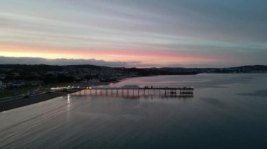 Paignton, Torbay, Güney Devon, İngiltere: DRONE ViEWS: Günbatımında Paignton Pier; Pier 1879 yılında Kraliçe Victoria 'nın saltanatı sırasında tamamlandı. Paignton, birçok farklı turizm merkeziyle popüler bir İngiltere tatil beldesidir (Clip 3).