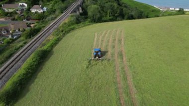 Broadbay, Torbay, Güney Devon, İngiltere: DRONE VİEWS: İHA, sürülen bir tarlada çimleri biçen bir traktörün kuş bakışı görüntüsünü verir. Devon, İngiltere 'de popüler bir tatil beldesidir ve tarım ve çiftlik hayvancılığıyla ünlüdür (Clip 4).
