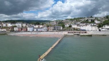 Dawlish, Güney Devon, İngiltere: DRONE VİEWS: Arka planda Dawlish kasabası şehir rıhtımının üzerinde drone daireleri olarak görülür; orta kısımda plaj ve ana hat tren yolu bulunur. Dawlish İngiltere 'de popüler bir tatil beldesidir (Clip 4).