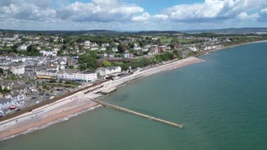 Dawlish, Güney Devon, İngiltere: DRONE VİEWS: Arka planda Dawlish kasabası şehir rıhtımının üzerinde drone daireleri olarak görülür; orta kısımda plaj ve ana hat tren yolu bulunur. Dawlish İngiltere 'de popüler bir tatil beldesidir (Clip 2).