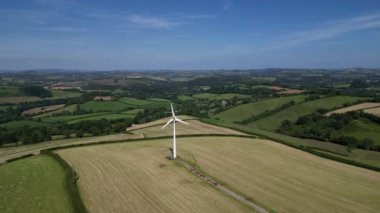 Rattery, Buckfastleigh, Devon, İngiltere yakınlarındaki DRONE VİEWS: İnsansız hava aracı kırsal ve tarım arazileriyle çevrili bir rüzgar türbininin etrafında dönüyor. Rüzgar türbinleri yenilenebilir enerjinin bir biçimidir ve 2030 yılına kadar net sıfır elde etmek için İngiltere makro stratejisinin bir parçasıdır (Clip 1).