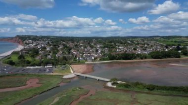 Budleigh Salterton, Doğu Devon, İngiltere: İHA arka planda Jurassic Sahili ve Budleigh Salterton 'u gösteren nehir samuru üzerinde bir köprü etrafında daireler çiziyor. Jurassic Coast popüler bir İngiltere turizm merkezidir (Clip 3).