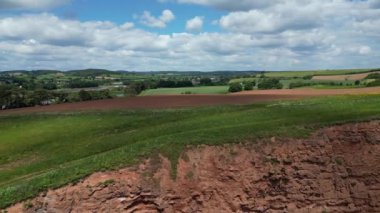 Budleigh Salterton, Doğu Devon, İngiltere: DRONE VİEWS: İHA, Jurassic Coast 'ta popüler bir tatil yeri olan Budleigh Salterton kasabası yakınlarındaki bir çiftlik arazisi ve nehir samuru ortaya çıkarmak için kızıl kumtaşı uçurumlarının üzerinden yükselir (Clip, 2.).