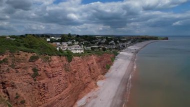 Budleigh Salterton, Doğu Devon, İngiltere: DRONE VİEWS: Dünya Mirası Jurassic Sahili 'nin bir kısmını oluşturan kırmızı kumtaşı uçurumları; B / g' deki Budleigh Salterton kasabası. Jurassic Coast popüler bir İngiltere turizm merkezidir (Clip 1).