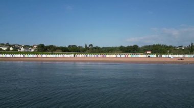 Goodrington Sands, Torbay, Güney Devon, İngiltere: DRONE VİEWS: İnsansız hava aracı deniz kenarındaki renkli sahil kulübelerine doğru alçaktan uçuyor. Torbay, birçok farklı ziyaretçi çekimleri bulunan popüler bir İngiltere tatil beldesidir (Clip 1).
