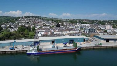 Teignmouth, Güney Devon, İngiltere: DRONE ViEW: Bir kargo gemisi liman kenarı yükleyicisi tarafından top kiliyle doldurulur. Teignmouth limanı ayrıca hayvan yemi, toplamı ve tuz ithalatını da alır; kasaba aynı zamanda popüler bir İngiltere tatil beldesidir (Clip 6). 