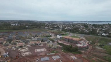 Paignton, Torbay, Güney Devon, İngiltere: DRONE ViEWS: İnsansız hava aracı White Rock yakınlarındaki yeşil kuşak arazisinde yapım aşamasındaki yeni bir konut inşaatı etrafında daireler çiziyor. Paignton, İngiltere 'de birçok turistik merkezi bulunan popüler bir tatil beldesidir (Clip 1).