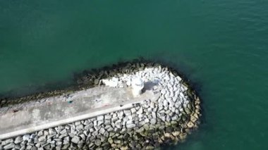 Brixham, Torbay, Güney Devon, İngiltere: DRONE VİEWS: Brixham deniz fenerinin ve liman duvarının eğimli bir görüntüsü; İHA, denize ve kıyı şeridine giden bir balıkçı teknesini ortaya çıkarmak için geri çekilir. Brixham bir balıkçılık limanıdır ve İngiltere 'de popüler bir tatil merkezidir (1).