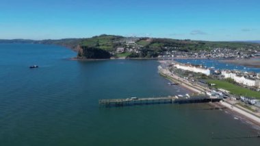 Teignmouth, Güney Devon, İngiltere: DRONE VİEWS: İnsansız hava aracı Grand Pier ve Teignmouth 'un arka planında The Ness' i, bir tarağı ve Teign Nehri 'ni gösteriyor. Teignmouth hem bir liman şehri hem de popüler bir İngiltere tatil beldesidir (Clip 3).