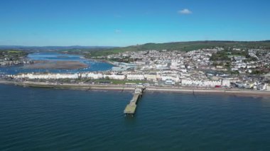 Teignmouth, Güney Devon, İngiltere: DRONE VİEWS: İnsansız hava aracı arka planda Teignmouth kasabasını ve Teign Nehri 'ni gösteren Grand Pier etrafında daireler çiziyor. Teignmouth hem bir liman şehri hem de popüler bir İngiltere tatil beldesidir (Clip 4).