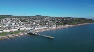 Teignmouth, Güney Devon, İngiltere: DRONE VİEWS: İnsansız hava aracı arka planda Teignmouth kasabasını ve doğuya bakan kıyı şeridini gösteren Grand Pier etrafında döner. Teignmouth hem liman şehri hem de İngiltere 'nin popüler tatil beldesidir..