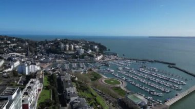 Torquay, Torbay, Güney Devon, İngiltere: DRONE VİEWS: İnsansız hava aracı yüzlerce demirli tekne ve yatı gösteren Torquay Marina 'dan uzaklaşıyor. Torquay popüler bir İngiltere tatil beldesi ve su sporları meraklıları için bir mıknatıstır (Clip 4).