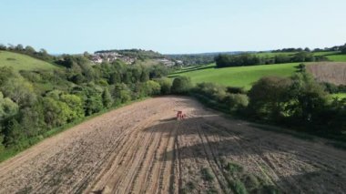 Blagdon, Torbay, Güney Devon, İngiltere: DRONE VİEWS: Bir tarla sürme makinesi bir tarım tarlasını sürer. Güney Devon, tarıma elverişli ve hayvancılık yapılan geniş tarım arazilerine sahip büyük bir tarım ilçesidir (Clip 1).