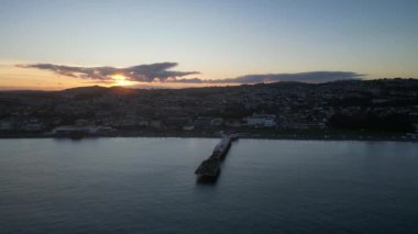Paignton, Torbay, Güney Devon, İngiltere: DRONE VİEWS: Paignton Pier günbatımına karşı set. İskele, Kraliçe Victoria 'nın saltanatı sırasında 1879 yılında tamamlandı. Paignton, birçok turistik etkinliği olan popüler bir İngiltere tatil beldesidir (Clip 5).