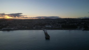 Paignton, Torbay, Güney Devon, İngiltere: DRONE VİEWS: Paignton Pier günbatımına karşı set. İskele, Kraliçe Victoria 'nın saltanatı sırasında 1879 yılında tamamlandı. Paignton, birçok turistik etkinliği olan popüler bir İngiltere tatil beldesidir (Clip 3).