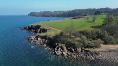 Broadbay, Torbay, Güney Devon, İngiltere: DRONE VİEWS: İHA Broadsand sahilindeki sahil kulübelerini göstermeden önce bir kıyı burnu üzerinde döner ve iner. Torbay, ünlü kıyı şeridi nedeniyle popüler bir İngiltere tatil beldesi..