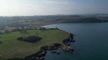 Broadbay, Torbay, Güney Devon, İngiltere: DRONE VİEWS: İHA, Broadsand sahiline doğru uçarken engebeli kıyı şeridi ve parkın üzerine iner. Güney Devon, İngiltere 'nin popüler tatil beldesidir..