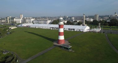 Plymouth, Devon, İngiltere: Plymouth Hoe 'daki Smeaton' s Tower deniz feneri; arka planda çeşitli savaş anıtları ve Plymouth şehir silueti bulunmaktadır. Deniz feneri 1759 'dan 1877' ye kadar çalıştı. Plymouth büyük bir Birleşik Krallık limanı ve deniz üssüdür.
