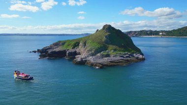 Torquay, Torbay, Güney Devon, İngiltere: DRONE ViEW: Turist teknesi Thatcher Kayası 'nın etrafında döner; Meadfoot plajı arka planda görülebilir. Torbay popüler bir İngiltere tatil beldesi ve su sporları meraklıları için bir mıknatıs..
