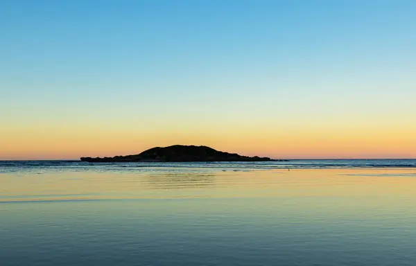 Sakin bir okyanusun üzerindeki altın gün batımı, gölge silueti doğadaki canlı gökyüzüne hafifçe zıt düşüyor..