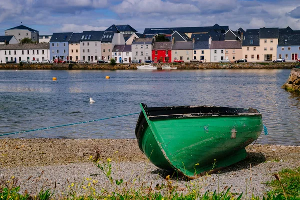 Arka planda Galway 'in silueti olan yeşil bir tekne kıyıda.