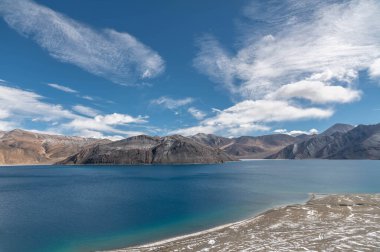 Hindistan 'ın Ladakh kentindeki el değmemiş yüksek irtifa gölü Pangong Tso' nun dramatik bulutları ve etrafındaki dağlarla nefes kesici manzarası. Macera seyahati temaları, doğa blogları, çevre kampanyaları ve Himalaya turizm promosyonları için mükemmel bir görsel..