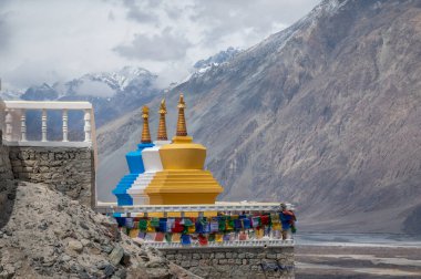 Ladakh, Hindistan 'da Maitreya Buddha' nın tabanında üç katmanlı renkli bir stupa. Himalayaların dramatik manzarasına karşı kurulan barış ve ruhaniliğin canlı bir sembolü..